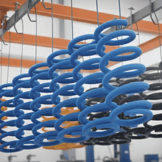 Línea de pintura electrostática industrial mostrando hileras de resortes de compresión en azul, amarillo y negro sobre una banda transportadora automatizada.